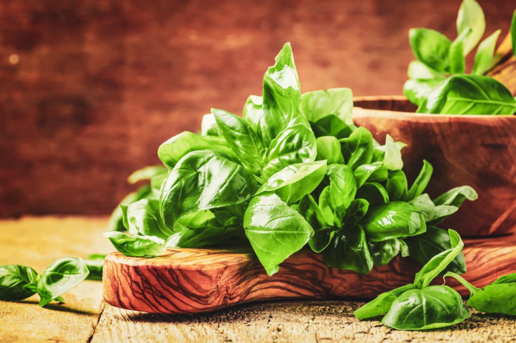 Picked leaves of basil piled onto a wooden board.